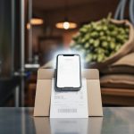 Close-up of a smartphone scanning a supplier beer receipt on a brewery workbench near stainless-steel tanks and ingredient supplies.